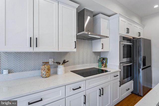 kitchen featuring wall chimney exhaust hood, white cabinetry, appliances with stainless steel finishes, light stone countertops, and backsplash
