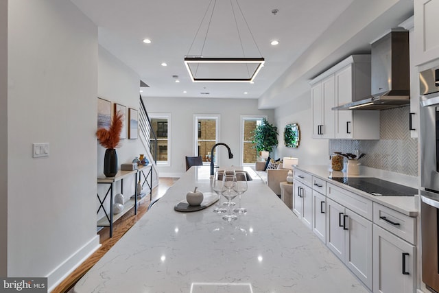 kitchen with sink, white cabinets, backsplash, black electric cooktop, and wall chimney exhaust hood