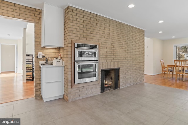 kitchen with double oven, light tile patterned flooring, white cabinetry, light countertops, and a brick fireplace