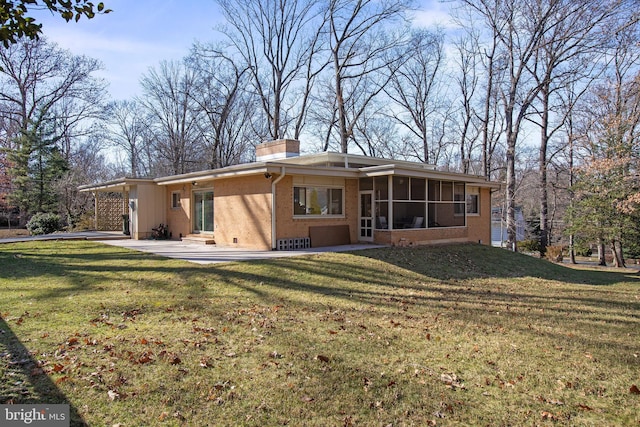 back of house with a yard, a sunroom, a chimney, and brick siding