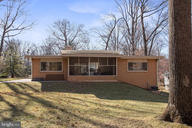 rear view of property with a yard, brick siding, a chimney, and a sunroom