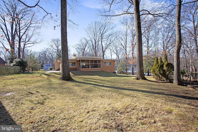 view of front of home with a sunroom, a chimney, fence, and a front lawn