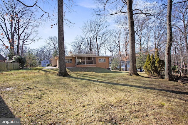 view of front of home with a sunroom, a chimney, fence, a front lawn, and brick siding