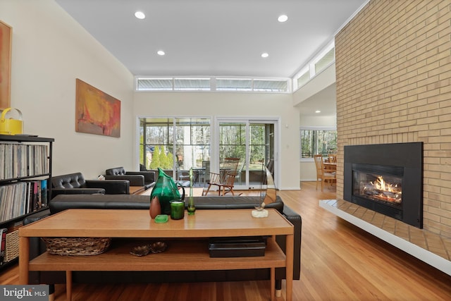 living area featuring a fireplace, a towering ceiling, light wood-style flooring, and recessed lighting