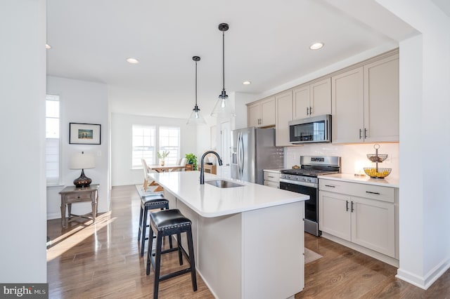 kitchen with sink, a kitchen island with sink, stainless steel appliances, decorative backsplash, and decorative light fixtures