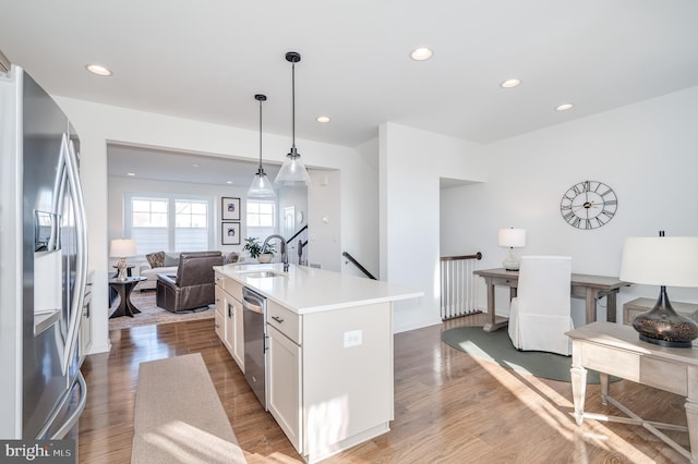 kitchen featuring sink, stainless steel appliances, an island with sink, white cabinets, and decorative light fixtures