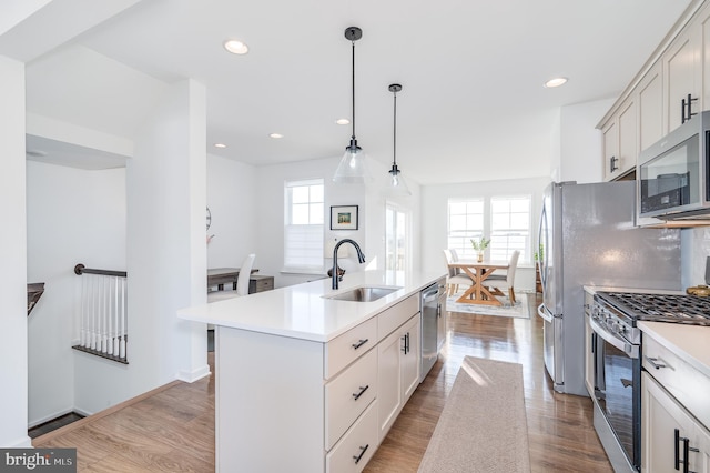 kitchen with pendant lighting, sink, a kitchen island with sink, stainless steel appliances, and a healthy amount of sunlight