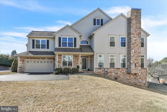 view of front facade with driveway, stone siding, a chimney, an attached garage, and a front lawn