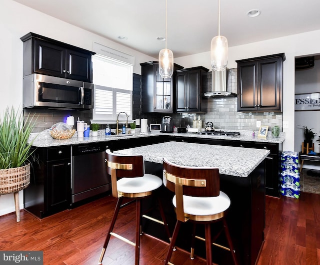 kitchen featuring a sink, hanging light fixtures, appliances with stainless steel finishes, a center island, and a kitchen bar