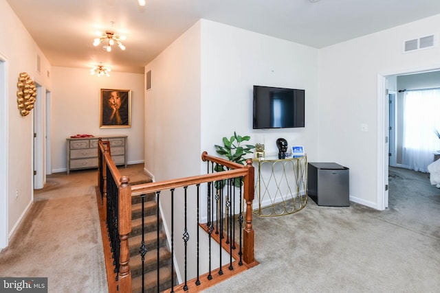 hallway with light carpet, visible vents, and an upstairs landing