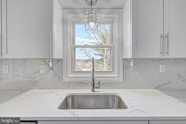 kitchen with sink, light stone counters, white cabinetry, hanging light fixtures, and decorative backsplash