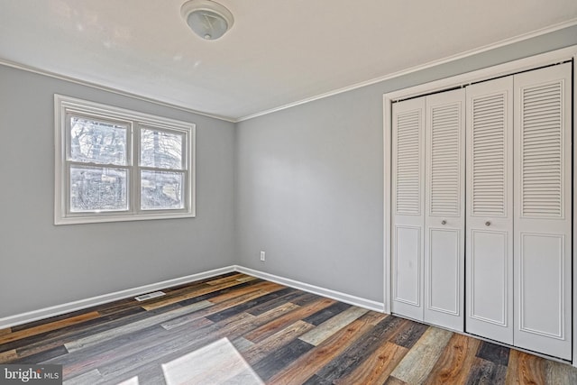 unfurnished bedroom with dark wood-type flooring, crown molding, and a closet