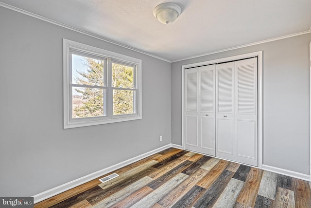 unfurnished bedroom featuring crown molding, dark hardwood / wood-style floors, and a closet