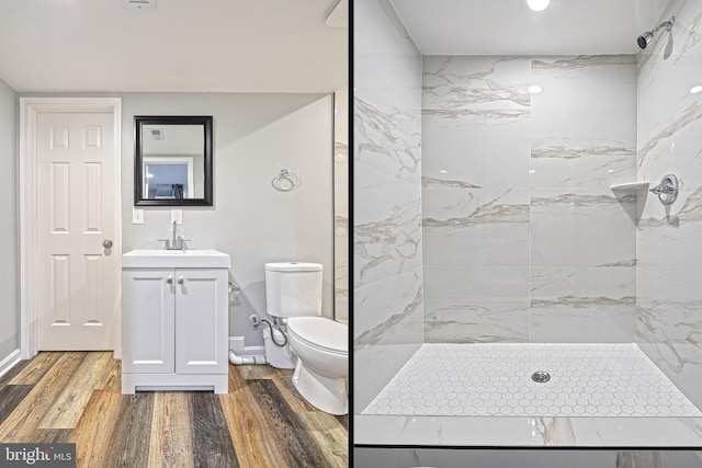 bathroom featuring a tile shower, vanity, wood-type flooring, and toilet