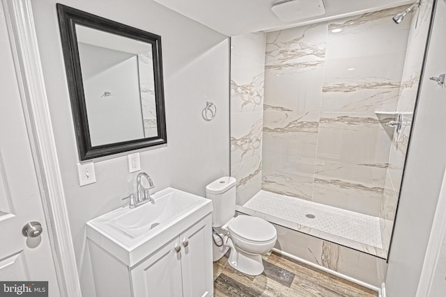 bathroom featuring hardwood / wood-style flooring, vanity, tiled shower, and toilet