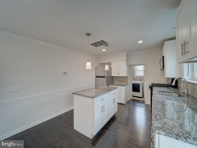 kitchen featuring white cabinetry, decorative light fixtures, appliances with stainless steel finishes, a kitchen island, and washer / clothes dryer