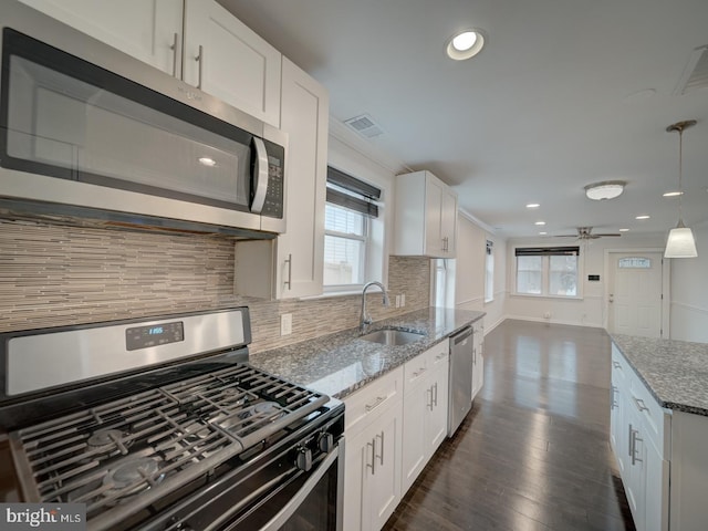 kitchen with appliances with stainless steel finishes, decorative light fixtures, white cabinetry, sink, and light stone countertops