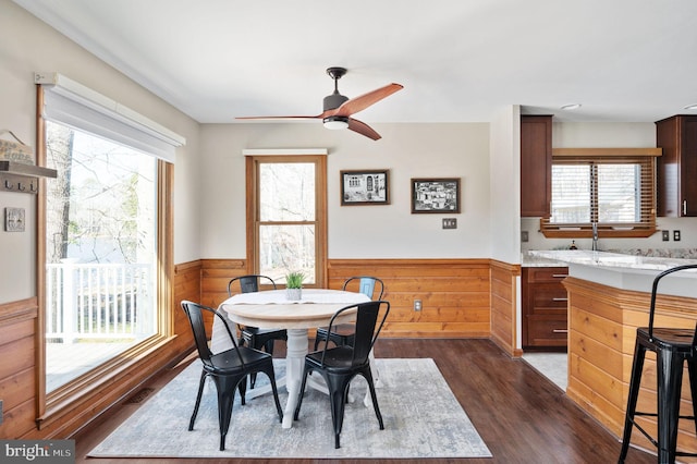 dining room featuring dark hardwood / wood-style floors, wooden walls, and ceiling fan