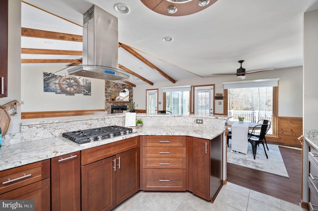 kitchen with light tile patterned floors, ceiling fan, light stone countertops, stainless steel gas cooktop, and island exhaust hood