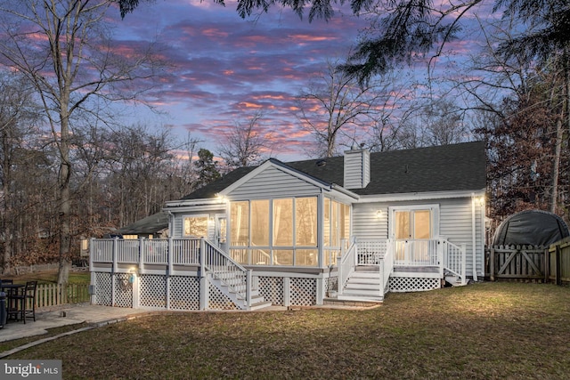 back house at dusk featuring a yard, a deck, and a sunroom