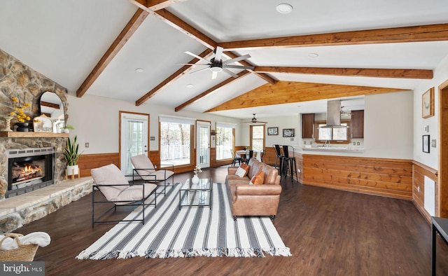 living room with lofted ceiling with beams, a stone fireplace, dark hardwood / wood-style floors, and ceiling fan