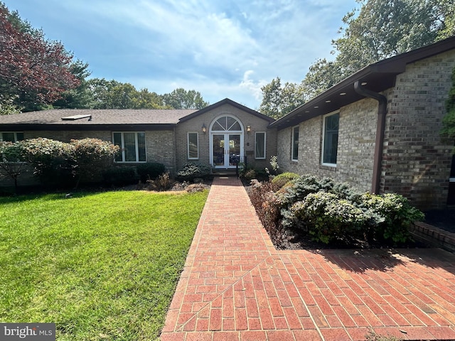 view of front of property featuring french doors, brick siding, and a front lawn