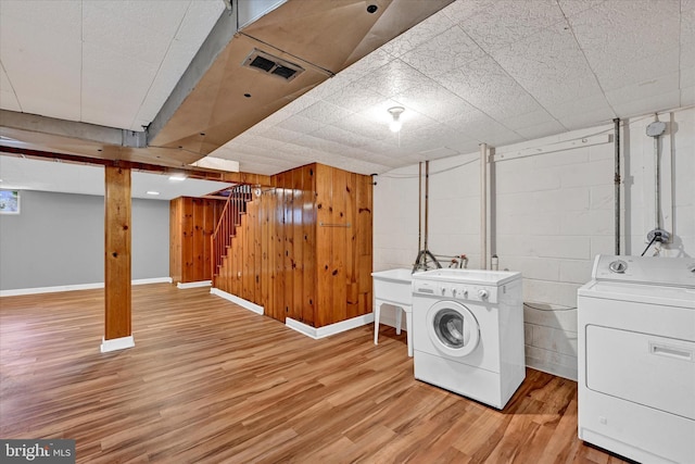 laundry area featuring wooden walls, washer and clothes dryer, and light hardwood / wood-style flooring