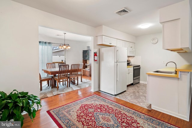 kitchen with sink, white cabinets, white appliances, and decorative light fixtures