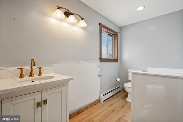 bathroom featuring wood-type flooring, toilet, vanity, and a baseboard heating unit