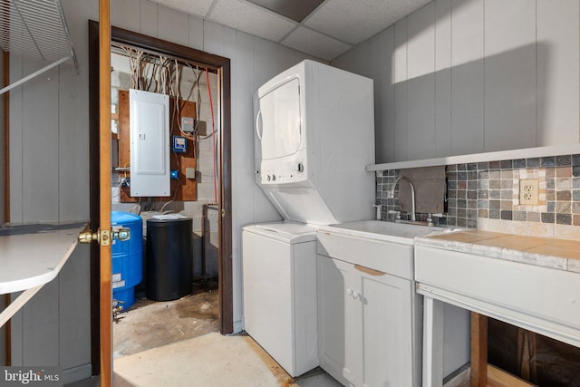 clothes washing area with stacked washing maching and dryer, sink, and electric panel