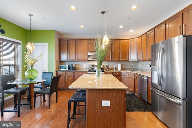 kitchen with pendant lighting, backsplash, a center island, stainless steel appliances, and light wood-type flooring