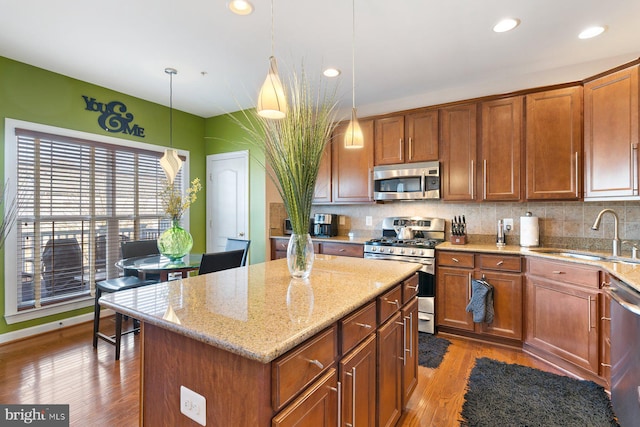 kitchen featuring sink, a kitchen island, pendant lighting, stainless steel appliances, and decorative backsplash