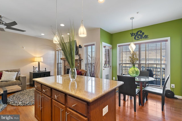 kitchen with decorative light fixtures, light hardwood / wood-style flooring, a kitchen island, ceiling fan, and light stone countertops