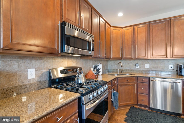 kitchen featuring sink, backsplash, stainless steel appliances, light stone countertops, and light wood-type flooring