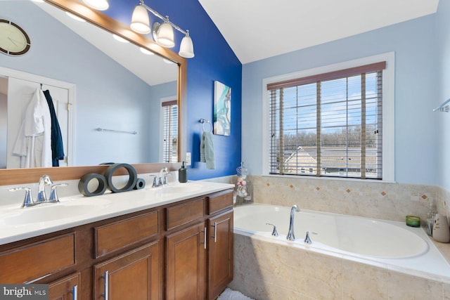 bathroom featuring vaulted ceiling, a relaxing tiled tub, and vanity