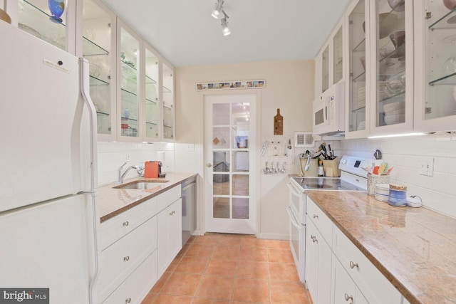 kitchen featuring backsplash, glass insert cabinets, light tile patterned floors, white appliances, and a sink