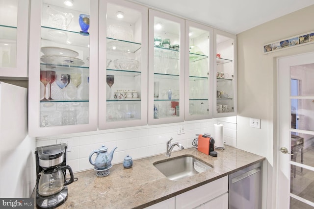 kitchen with a sink, tasteful backsplash, white cabinets, glass insert cabinets, and dishwasher