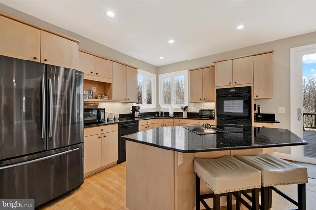 kitchen featuring recessed lighting, light brown cabinetry, black appliances, light wood-style floors, and a kitchen bar