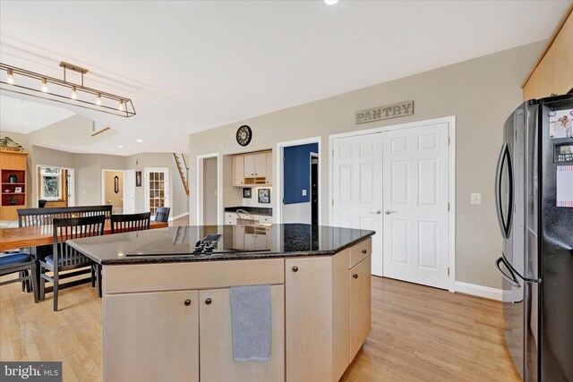 kitchen with dark stone countertops, a kitchen island, freestanding refrigerator, and light wood-style floors