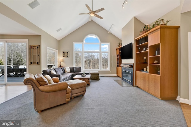 living area featuring baseboards, a fireplace with flush hearth, high vaulted ceiling, and ceiling fan