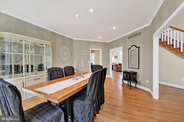 dining area featuring baseboards, visible vents, light wood-style flooring, stairs, and crown molding