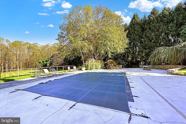 view of swimming pool with a covered pool, a wooded view, and a patio area