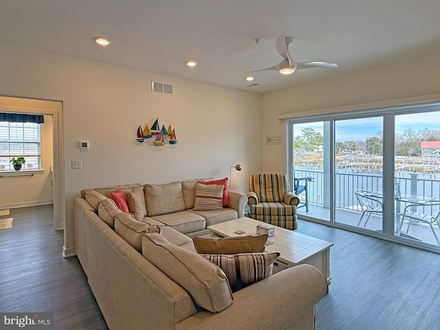 living room featuring dark wood-type flooring, ceiling fan, and plenty of natural light