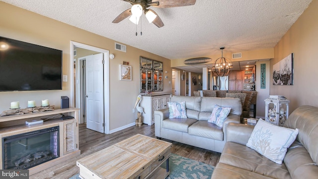 living room featuring dark hardwood / wood-style flooring, ceiling fan with notable chandelier, and a textured ceiling