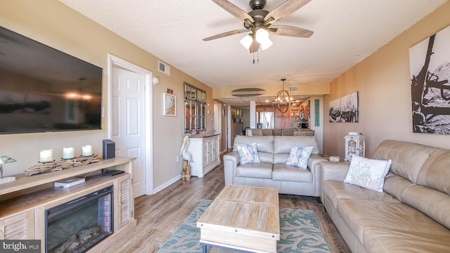 living room featuring ceiling fan with notable chandelier, a textured ceiling, and light wood-type flooring