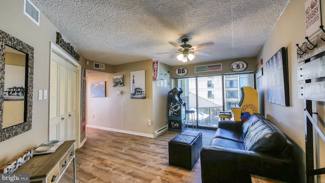 living room featuring baseboard heating, ceiling fan, wood-type flooring, and a textured ceiling