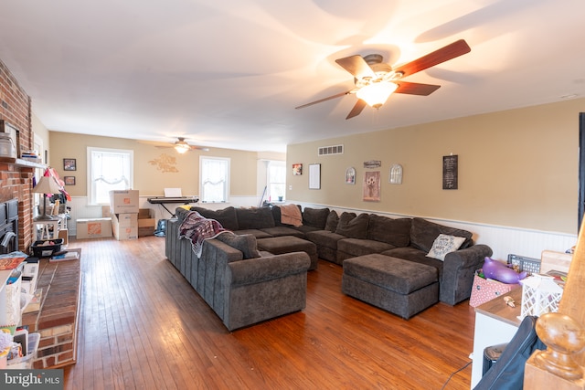 living room featuring wood-type flooring, a brick fireplace, and ceiling fan