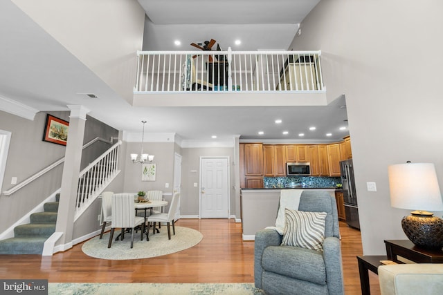 living room with crown molding, stairway, light wood-style floors, and visible vents