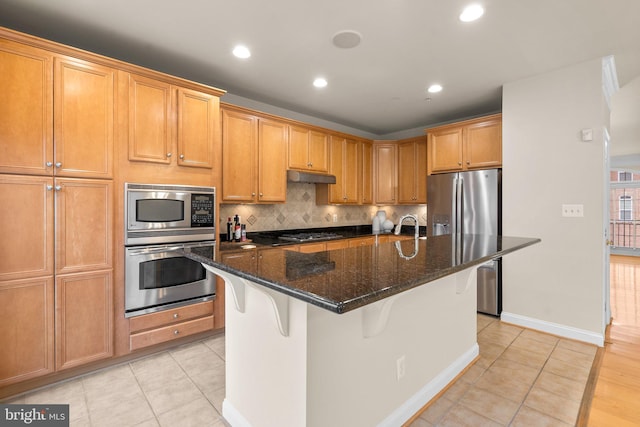 kitchen featuring stainless steel appliances, a kitchen breakfast bar, an island with sink, and dark stone counters