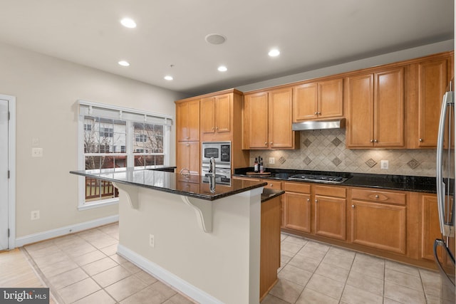 kitchen with an island with sink, light tile patterned floors, backsplash, and dark stone counters